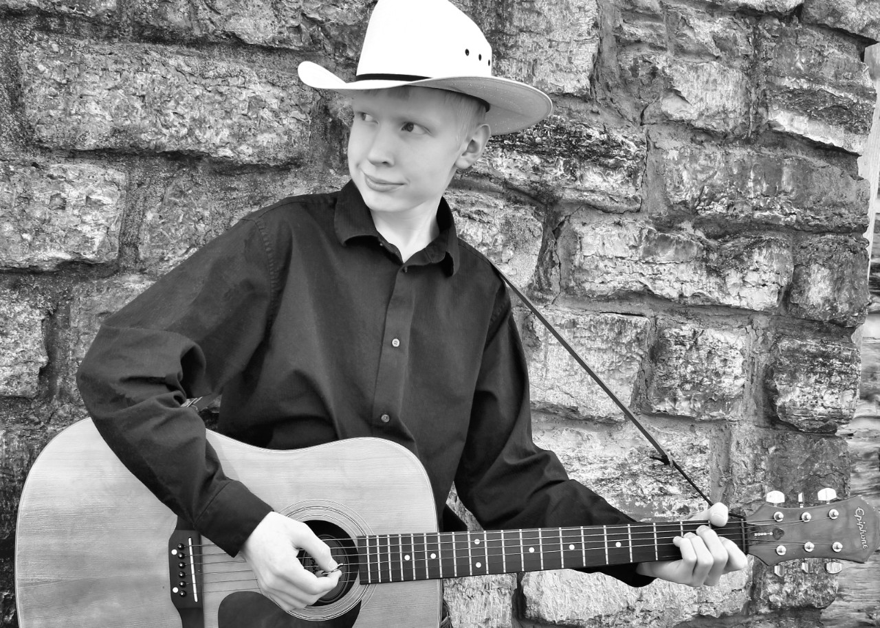 Andrew Braach The photo of Andrew in this article is a black and white photo of a young man with light blond hair, a black button up shirt and jeans, and a cowboy hat. It looks like a professional headshot of a musician – he is leaning against a stone wall looking off to the left past the camera, smiling slightly and holding a guitar as though he is about to play.