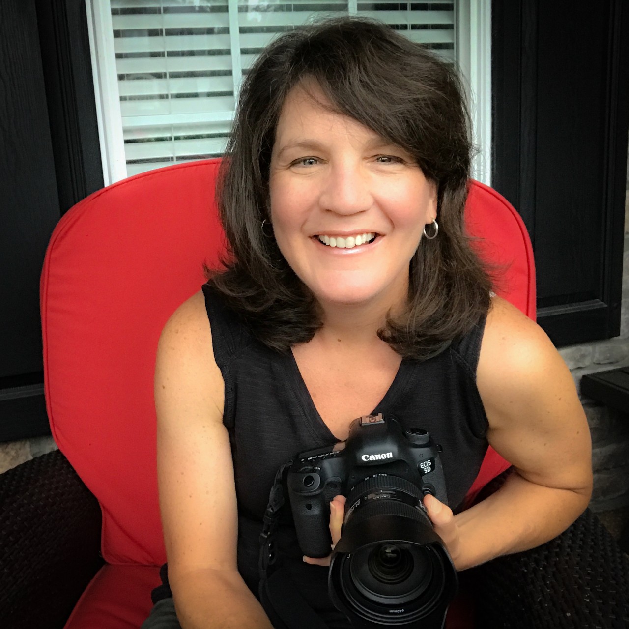 Jen Vogus, self-portrait self-portrait of the article author and photographer, Jen Vogus. She is seated in a red chair holding very large camera with a big lens.