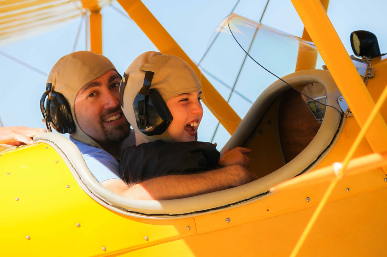 Photo by Jen Vogus a boy and an older man in the cockpit of a yellow plane. Both males are smiling happily.