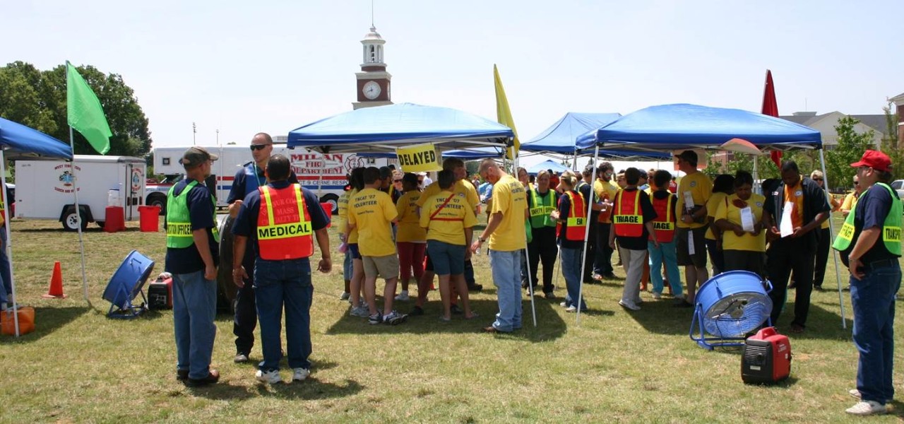 People  participating in a large exercise outside under several pop-up canopy tents